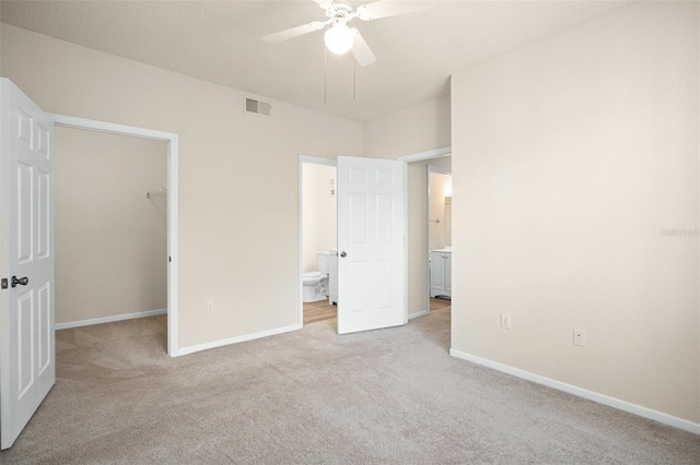 unfurnished bedroom with connected bathroom, a spacious closet, ceiling fan, light carpet, and a closet