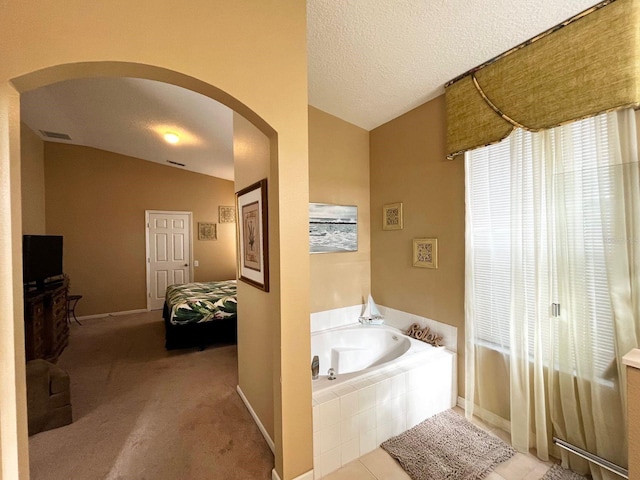 bathroom featuring a textured ceiling, tiled bath, and vaulted ceiling