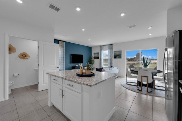 kitchen featuring stainless steel fridge, a center island, light tile patterned floors, and white cabinets