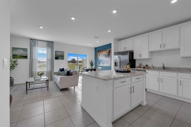 kitchen with light tile patterned floors, stainless steel fridge, white cabinetry, a center island, and light stone countertops