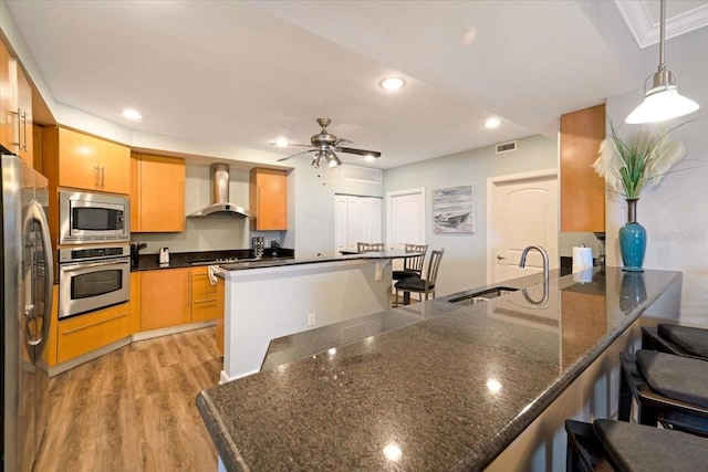 kitchen featuring pendant lighting, sink, wall chimney exhaust hood, a kitchen bar, and stainless steel appliances