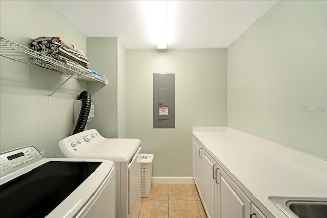 clothes washing area featuring electric panel, washer and dryer, light tile patterned floors, and cabinets