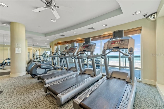 exercise room featuring a tray ceiling, ceiling fan, and light colored carpet