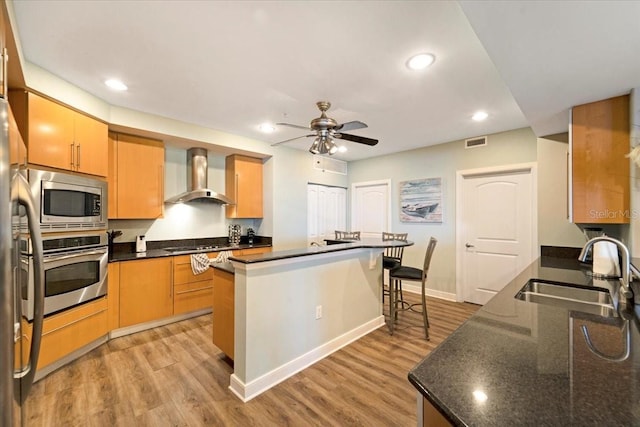 kitchen with a center island, wall chimney range hood, sink, appliances with stainless steel finishes, and light hardwood / wood-style floors