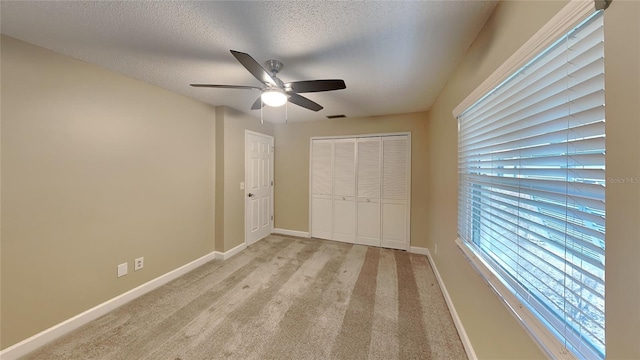 unfurnished bedroom featuring ceiling fan, a closet, light colored carpet, and a textured ceiling