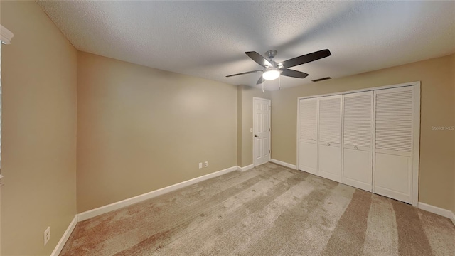 unfurnished bedroom featuring light carpet, a textured ceiling, a closet, and ceiling fan