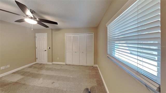 unfurnished bedroom featuring ceiling fan, a closet, light colored carpet, and a textured ceiling