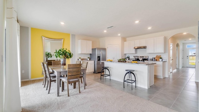 kitchen featuring white cabinets, appliances with stainless steel finishes, a center island with sink, and light carpet