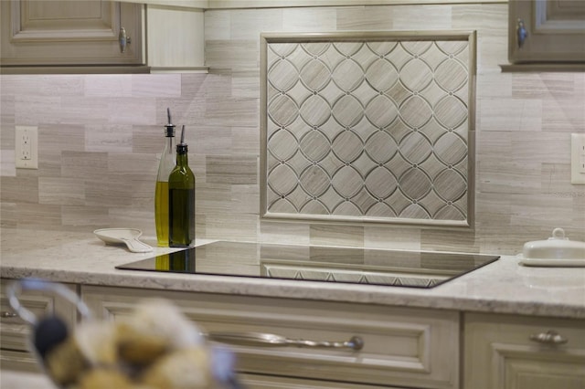 kitchen featuring decorative backsplash, black electric stovetop, cream cabinetry, and light stone counters