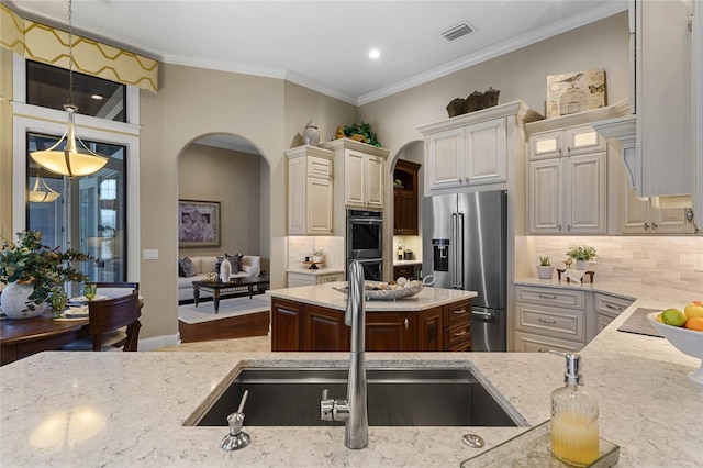 kitchen featuring stainless steel appliances, light stone counters, crown molding, decorative light fixtures, and decorative backsplash