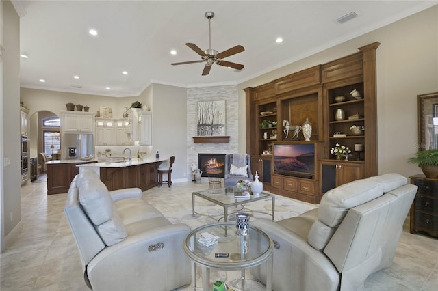 tiled living room with a large fireplace, ceiling fan, crown molding, and sink