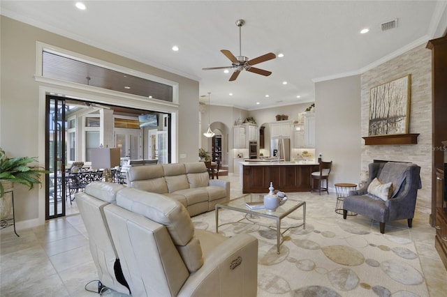 tiled living room with a fireplace, ceiling fan, and crown molding