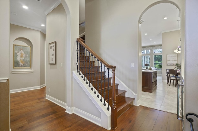 staircase with wood-type flooring and ornamental molding