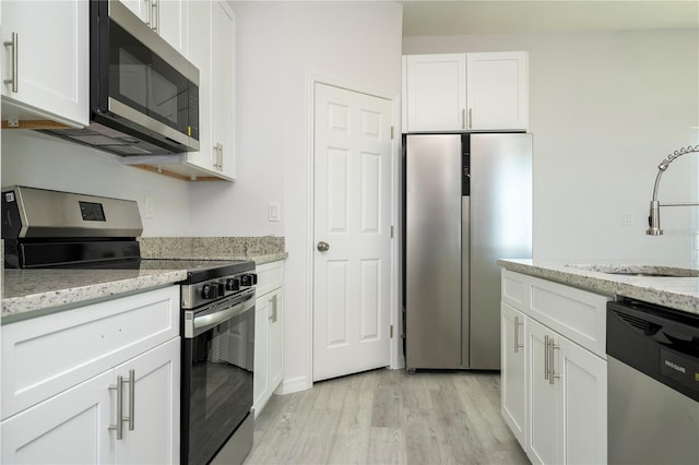 kitchen featuring sink, light wood-type flooring, appliances with stainless steel finishes, light stone counters, and white cabinetry