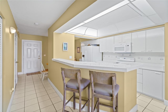 kitchen with white cabinets, a kitchen breakfast bar, white appliances, and light tile patterned floors