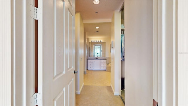 hallway featuring a textured ceiling, light colored carpet, and sink