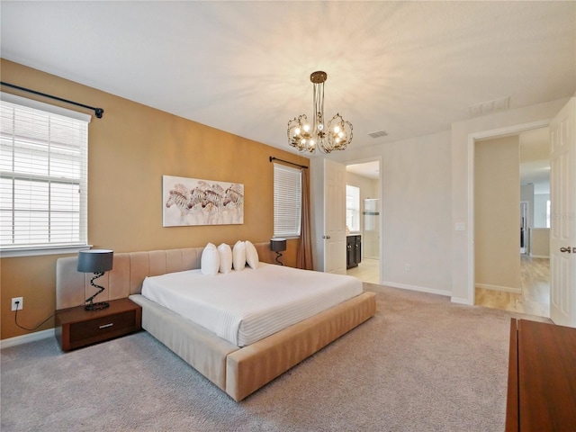 bedroom with ensuite bathroom, light colored carpet, and a chandelier