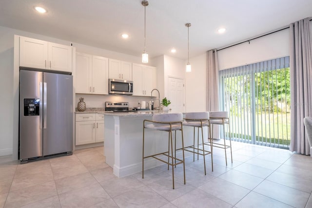 kitchen featuring pendant lighting, light stone countertops, an island with sink, appliances with stainless steel finishes, and white cabinetry