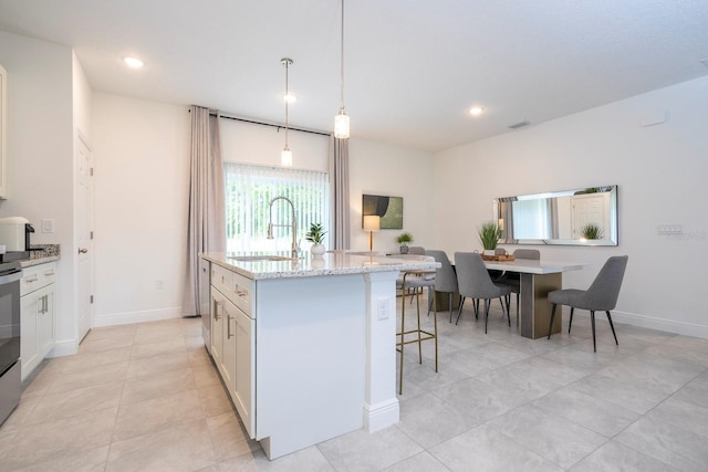 kitchen featuring a center island with sink, white cabinets, sink, decorative light fixtures, and light stone counters