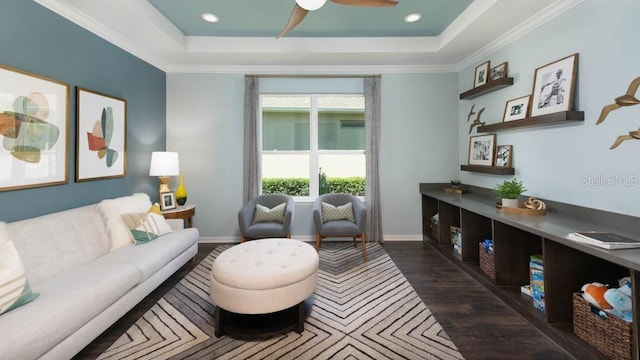 living room featuring ceiling fan, a raised ceiling, ornamental molding, and dark wood-type flooring