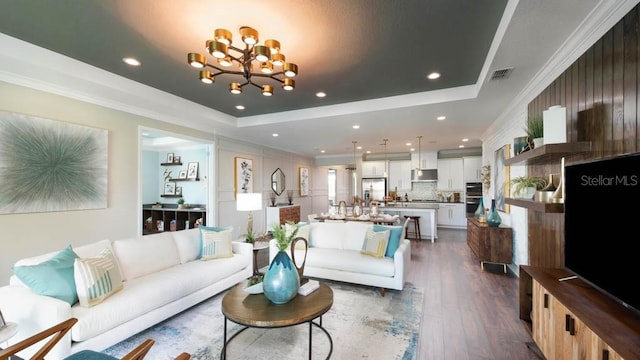 living room with dark hardwood / wood-style floors, a raised ceiling, crown molding, and an inviting chandelier