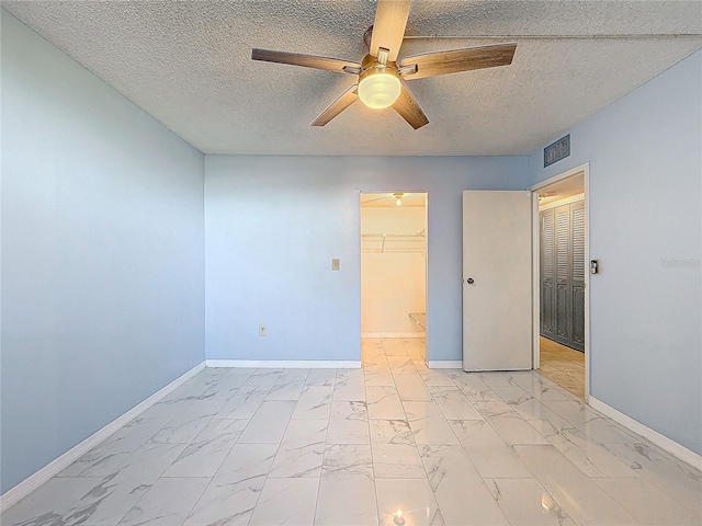 unfurnished bedroom with a textured ceiling, a walk in closet, a closet, and ceiling fan