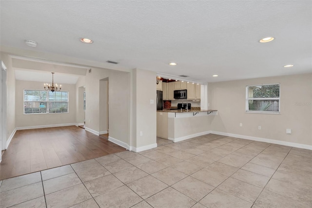 unfurnished living room with light wood-type flooring, a textured ceiling, and a chandelier