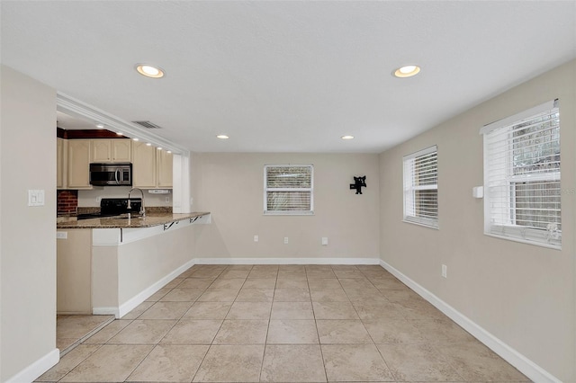 kitchen featuring kitchen peninsula, black range oven, dark stone counters, and light tile patterned floors