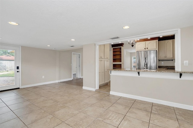 kitchen with a textured ceiling, light tile patterned flooring, light stone counters, kitchen peninsula, and stainless steel refrigerator