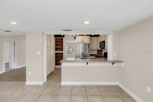 kitchen with kitchen peninsula, a textured ceiling, stainless steel appliances, and light stone counters