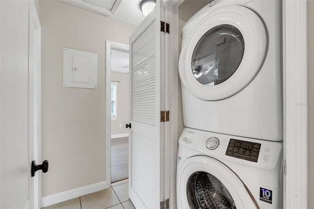 washroom with light tile patterned floors, stacked washer / dryer, and electric panel