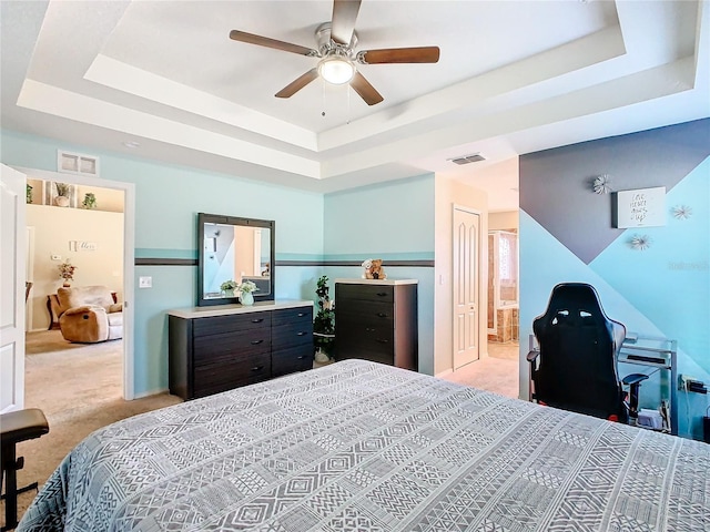 bedroom with light colored carpet, a raised ceiling, ceiling fan, and ensuite bathroom