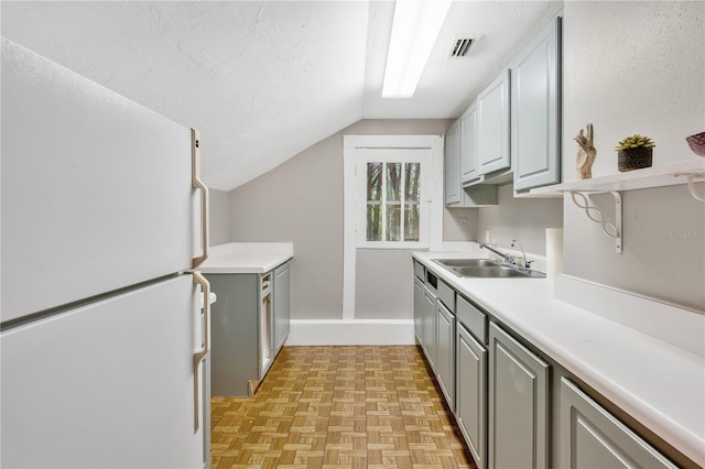 kitchen featuring gray cabinetry, white refrigerator, sink, vaulted ceiling, and light parquet flooring