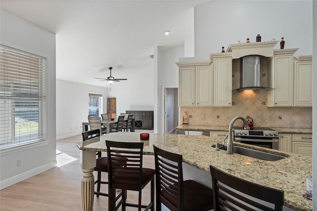 kitchen with light stone counters, wall chimney exhaust hood, light hardwood / wood-style floors, and cream cabinetry