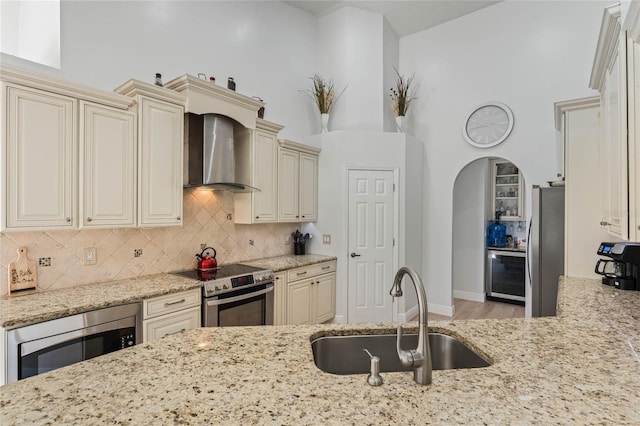 kitchen featuring wall chimney exhaust hood, sink, stainless steel appliances, and cream cabinets