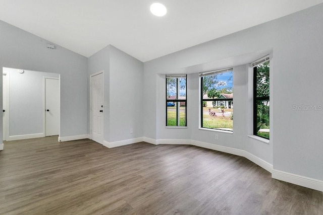 empty room with plenty of natural light, dark hardwood / wood-style flooring, and vaulted ceiling