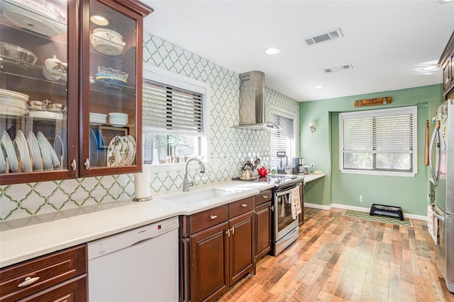 kitchen with backsplash, wall chimney range hood, sink, light hardwood / wood-style floors, and stainless steel appliances