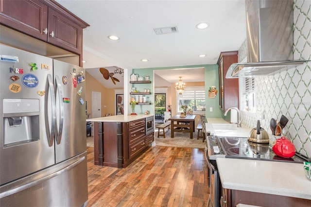 kitchen with sink, stainless steel appliances, wall chimney range hood, a chandelier, and wood-type flooring