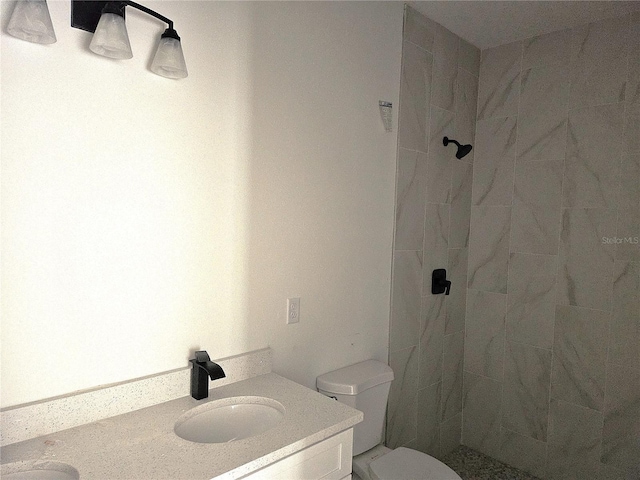 bathroom featuring a tile shower, vanity, and toilet