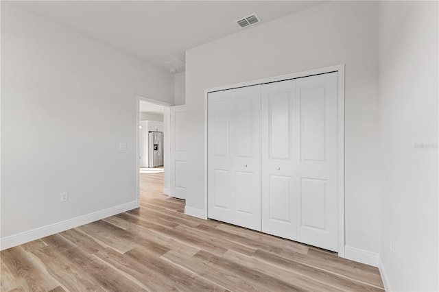 unfurnished bedroom with light hardwood / wood-style floors, stainless steel refrigerator with ice dispenser, and a closet