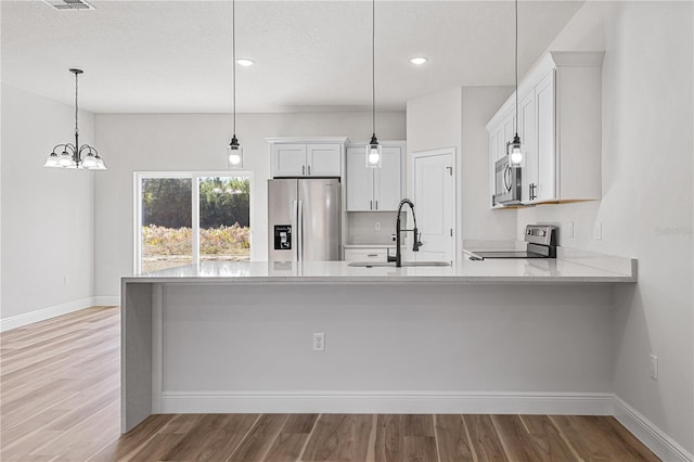 kitchen featuring pendant lighting, light wood-type flooring, stainless steel appliances, and white cabinetry