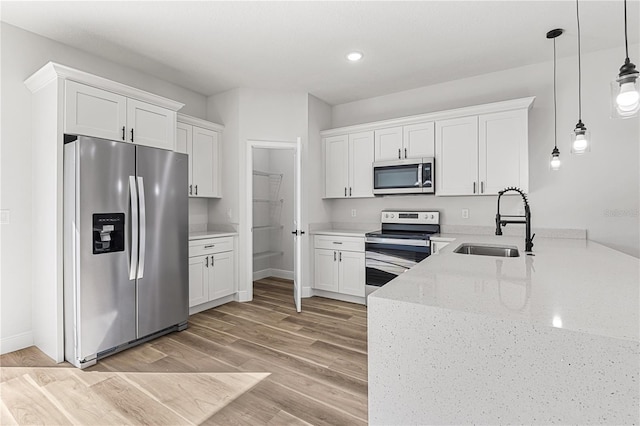 kitchen featuring appliances with stainless steel finishes, light wood-type flooring, sink, decorative light fixtures, and white cabinetry