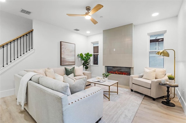 living room with a tiled fireplace, light hardwood / wood-style floors, and ceiling fan