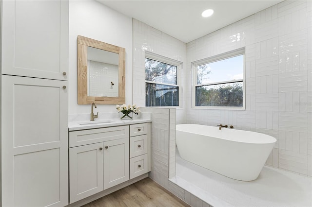 bathroom with wood-type flooring, tile walls, vanity, and a tub to relax in