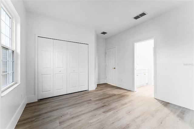 unfurnished bedroom with a closet, light hardwood / wood-style floors, and multiple windows