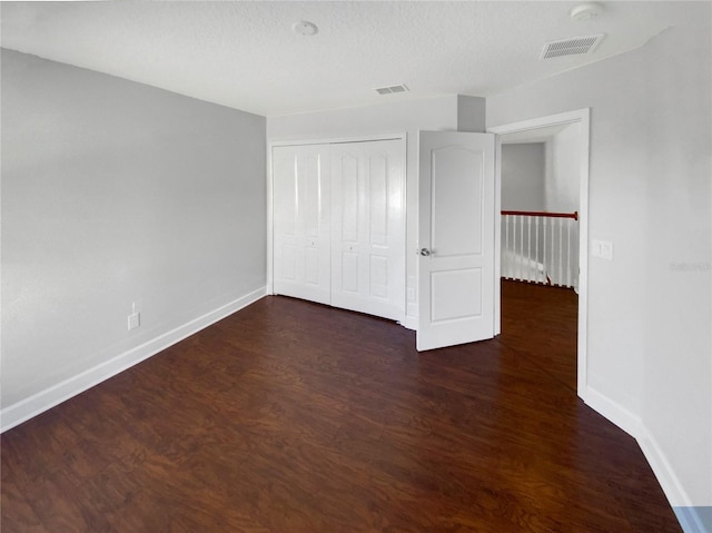 unfurnished bedroom featuring dark hardwood / wood-style flooring, a textured ceiling, and a closet