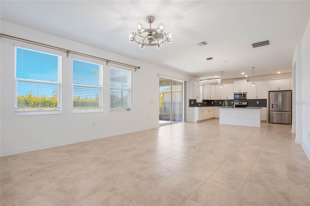 interior space with appliances with stainless steel finishes, a kitchen island, decorative light fixtures, an inviting chandelier, and white cabinetry