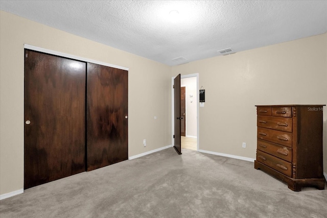 unfurnished bedroom featuring light carpet, a closet, and a textured ceiling