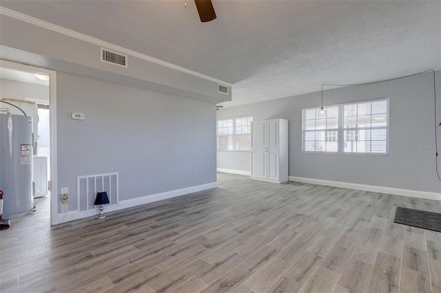 empty room featuring water heater, ceiling fan, light hardwood / wood-style floors, and a textured ceiling