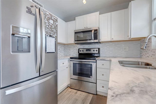 kitchen featuring white cabinets, sink, light wood-type flooring, light stone counters, and stainless steel appliances